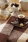 A cup of cappuccino on a brown checked table cloth