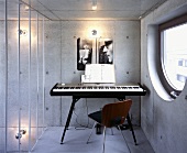 A music room with a keyboard and a chair against an exposed concrete wall
