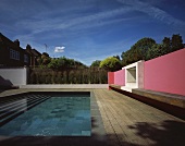 Modern architecture - a pink wall with a wooden bench in front of a pool