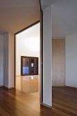 A modern anteroom with parquet flooring and an open doorway with a view into an empty room