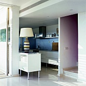 A living room with an open-plan kitchen and white cupboards