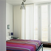A modern bedroom with striped bedclothes on a double bed with curtains at the window