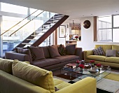 Different coloured sofas in front of a glass table with an open staircase in an open-plan living room