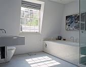 A white designer bathroom with stone tiles on the bathtub and white mosaic floor tiles