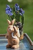 A clay rabbit figure in front of purple hyacinths in a glass