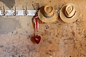 Straw hats and a glass heart on an old row of hooks