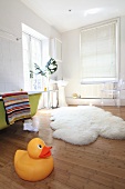 A giant rubber duck and a sheepskin rug on a the floor in a bathroom with a green, free-standing bathtub