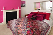A double bed with decorative cushions and a quilt in a bedroom with pink and white walls