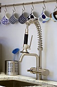 Cups hanging from hooks above a kitchen tap