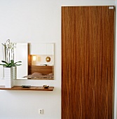 An orchid on a small shelf in front of a wall mirror next to a bedroom door