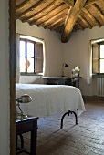 A view into a bedroom with a terracotta floor and a wood beam ceiling