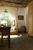 A dining table and chairs and a rattan sofa in front of an arched window in a dining room