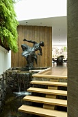 A small waterfall and a sculpture next to a flight of floating stairs in an entrance way