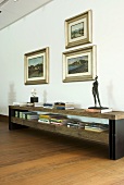 Books and sculptures on a sideboard with framed pictures hanging above