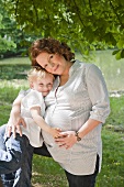 A little girl cuddling her pregnant mother by a lake