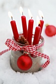 Rote Kerzen in einem Einmachglas mit Geschenkband und Weihnachtskugel im Schnee