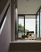 Beistelltisch aus Holz neben Sessel mit schwarz lackierter geschwungener Sitzfläche aus Bauhauszeit vor offener Terrasse