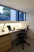 Modern home office under a bank of windows with a retro table lamp beside a Notebook computer