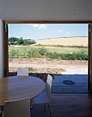 Dining table with white chairs in front of open patio doors with a view of a sunny garden