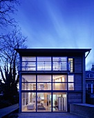 Contemporary home in the twilight with glass facade and a view of illuminated floors