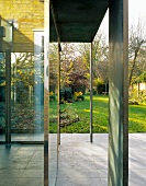 Scheibenartige Stahlstützen vor Haus mit Glasfassade und Blick in sonnigen Garten