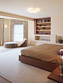 Double bed with light brown bed linen and modern divan in front of built-in shelves in a spacious bedroom