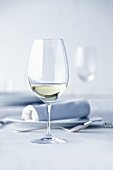 Glas Weißwein auf weiss gedecktem Tisch