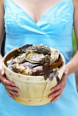 Woman holding fresh oysters in woodchip basket