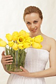 A woman holding a glass vase filled with yellow tulips