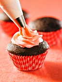 A chocolate cupcake being decorated with cream