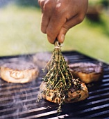 Beef fillets on a barbecue being rubbed with thyme