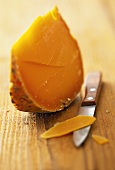 Mimolette (semi-hard cheese) on wooden background with knife