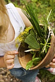 Child holding wooden bowl of fresh herbs in garden