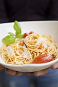 Hands holding plate of spaghetti with tomatoes & Parmesan