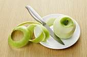 Peeled green apple with apple peel on plate