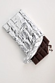 Bar of chocolate in silver paper, with a piece broken off