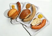 Assorted sausages with mustard and roll on paper plate