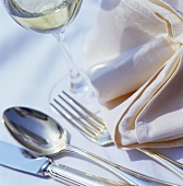 Cutlery with fabric napkin and a glass of white wine