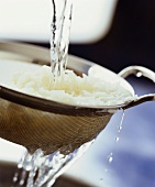 Gekochter Reis wird im Sieb abgewaschen