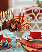 Red candles in a wine glass with small rose hip wreath
