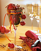 Weinglas mit roten Äpfeln, Hagebutten und Moos gefüllt