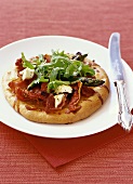 Mini-pizza with dried tomatoes, prosciutto and rocket