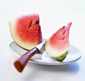 Two pieces of watermelon on a plate with knife