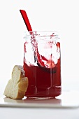 A jar of raspberry jelly with spoon and slice of bread