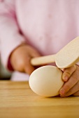 Kleine Mädchenhände halten einen Holzkochlöffel und ein Ei