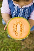 Small girl holding half a cantaloupe melon
