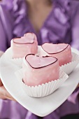 Woman holding three pink heart-shaped petit fours on plate