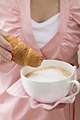 Frau hält grosse Tasse Cappuccino und Croissant