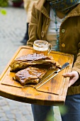 Woman holding glazed ribs and glass of beer on board