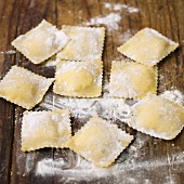 Home-made ravioli with flour on wooden background